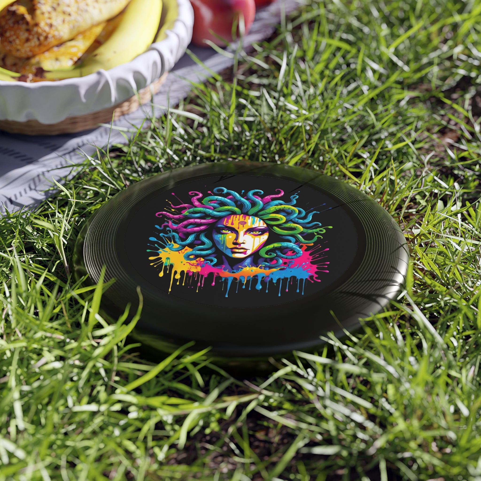 Colorful Medusa illustration on a black background, next to a picnic setup, showcasing the vibrant Neon Medusa Flying Disc.