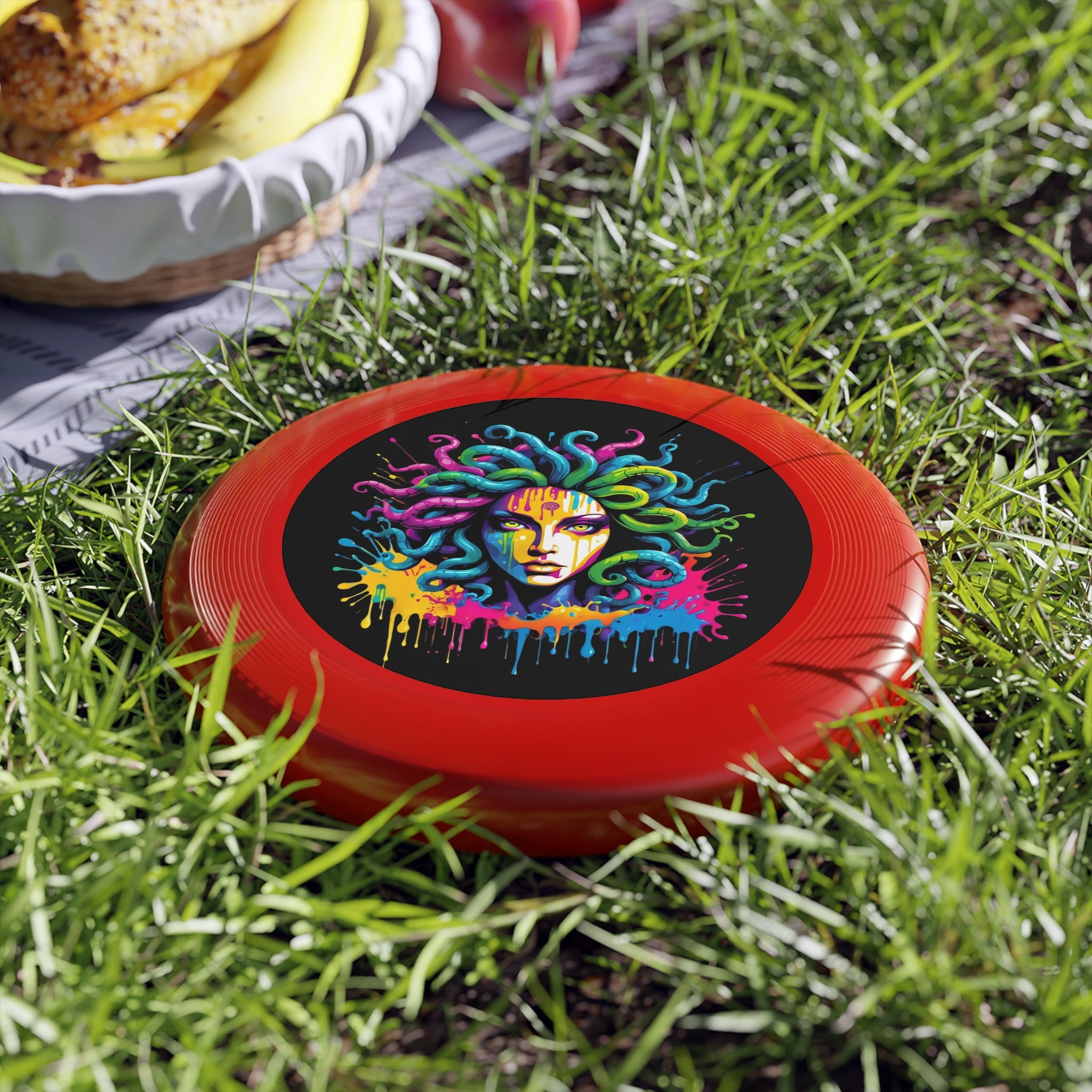 Vibrant Medusa Flying Disc on grass with a picnic setup, featuring graffiti-inspired colors on a red background.