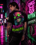 The vibrant all-over print T-shirt features a steampunk-inspired rider with a paint-splattered top hat and teal hair, set against a colorful background of fluorescent pink, green, and teal. The model showcases the shirt in an urban setting with neon lights, highlighting the striking 'Retrofitted Revolution' artwork on the back.