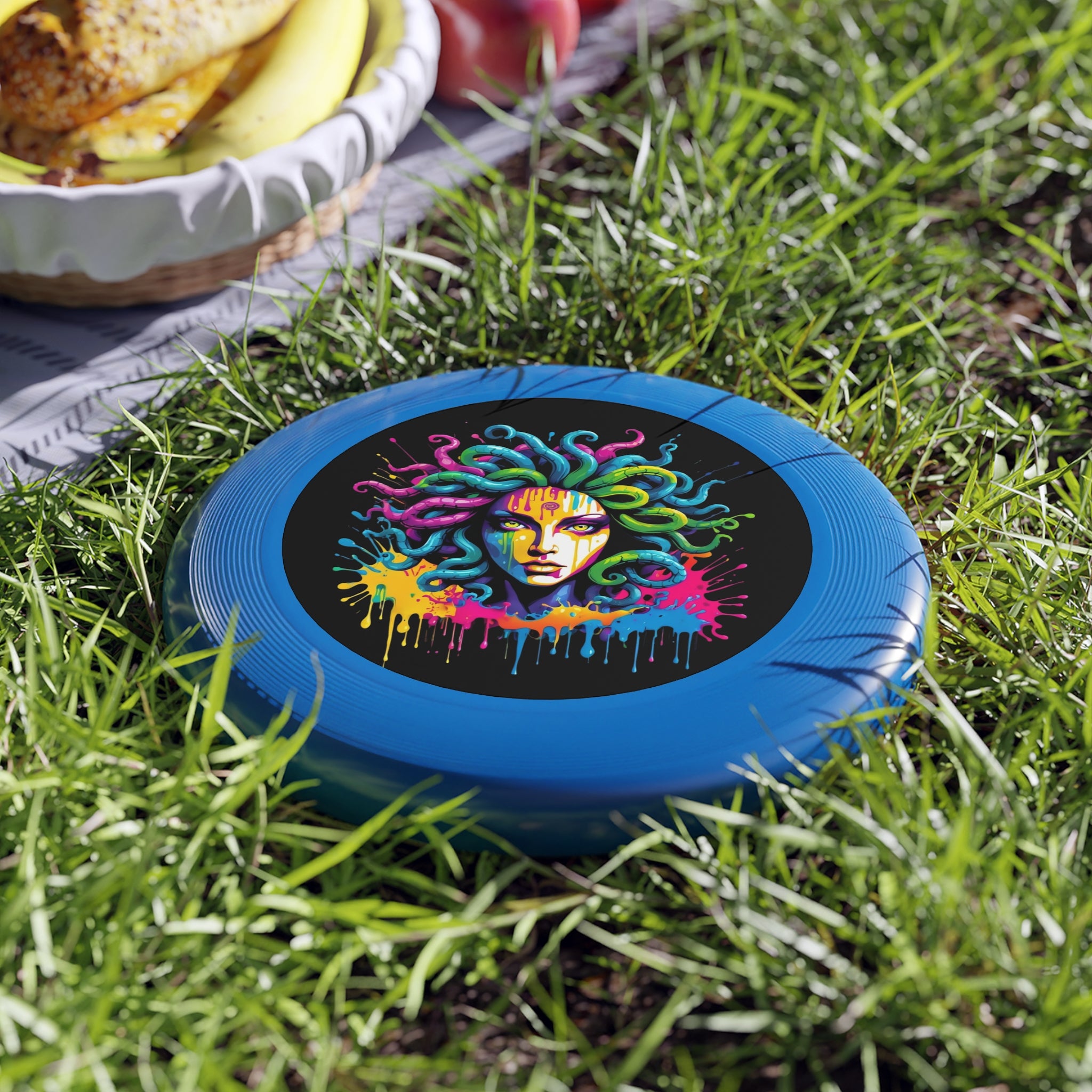 Colorful Medusa Flying Disc with graffiti-inspired design, set on green grass next to a picnic with fruits.