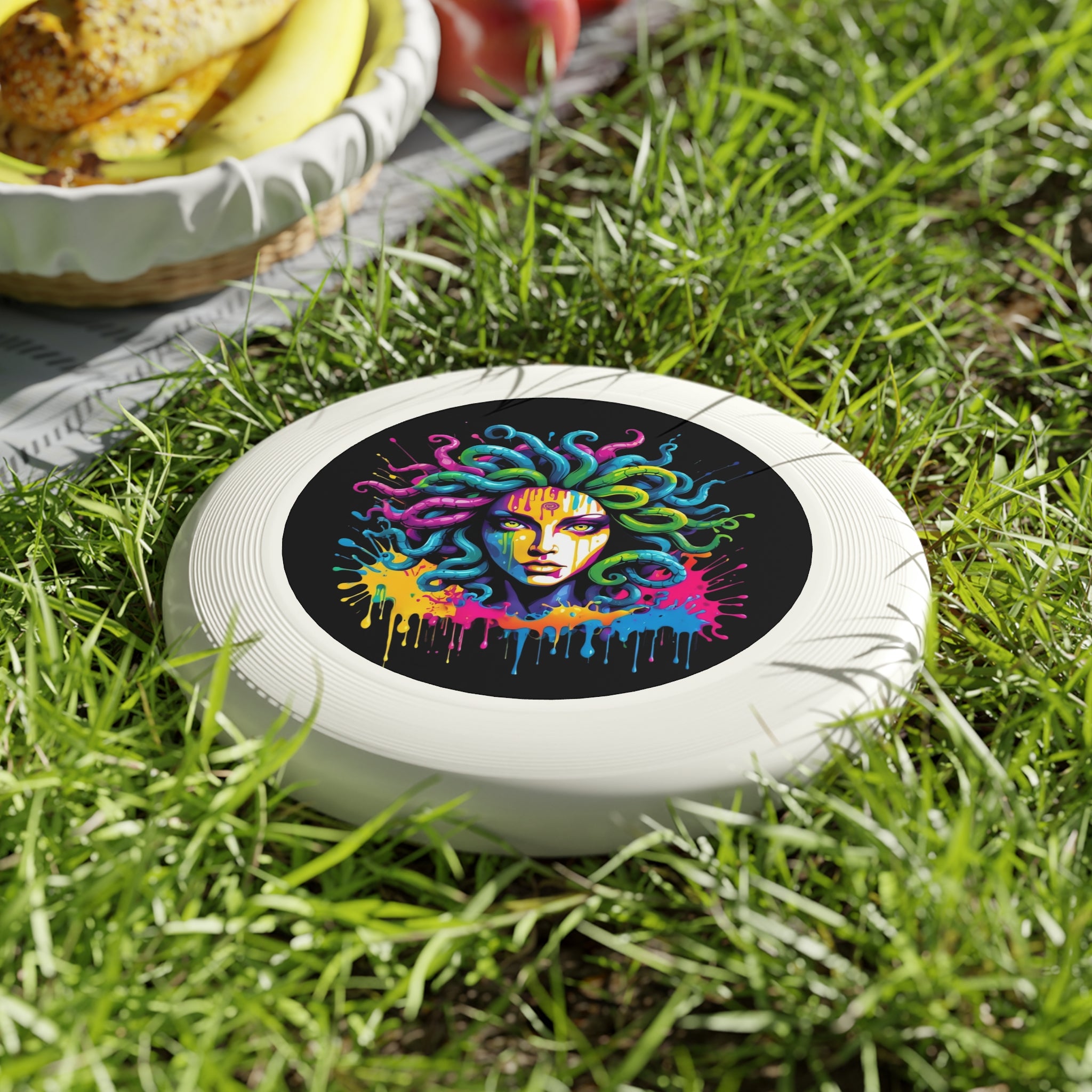 Colorful Medusa flying disc on grass next to a basket of fruit, perfect for outdoor fun and games.