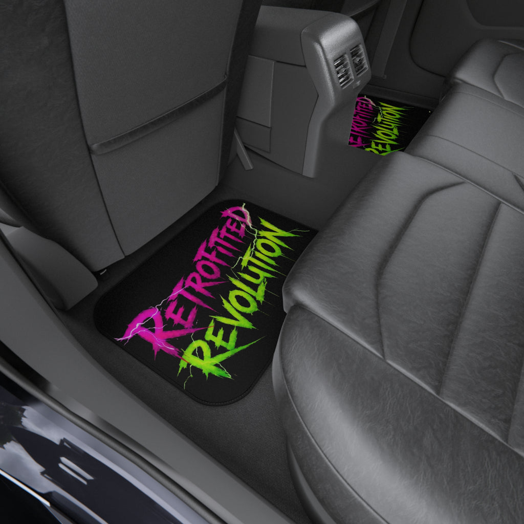 Car mats featuring vibrant graffiti-style "RETROFITTED REVOLUTION" text in a vehicle interior with dark upholstery.