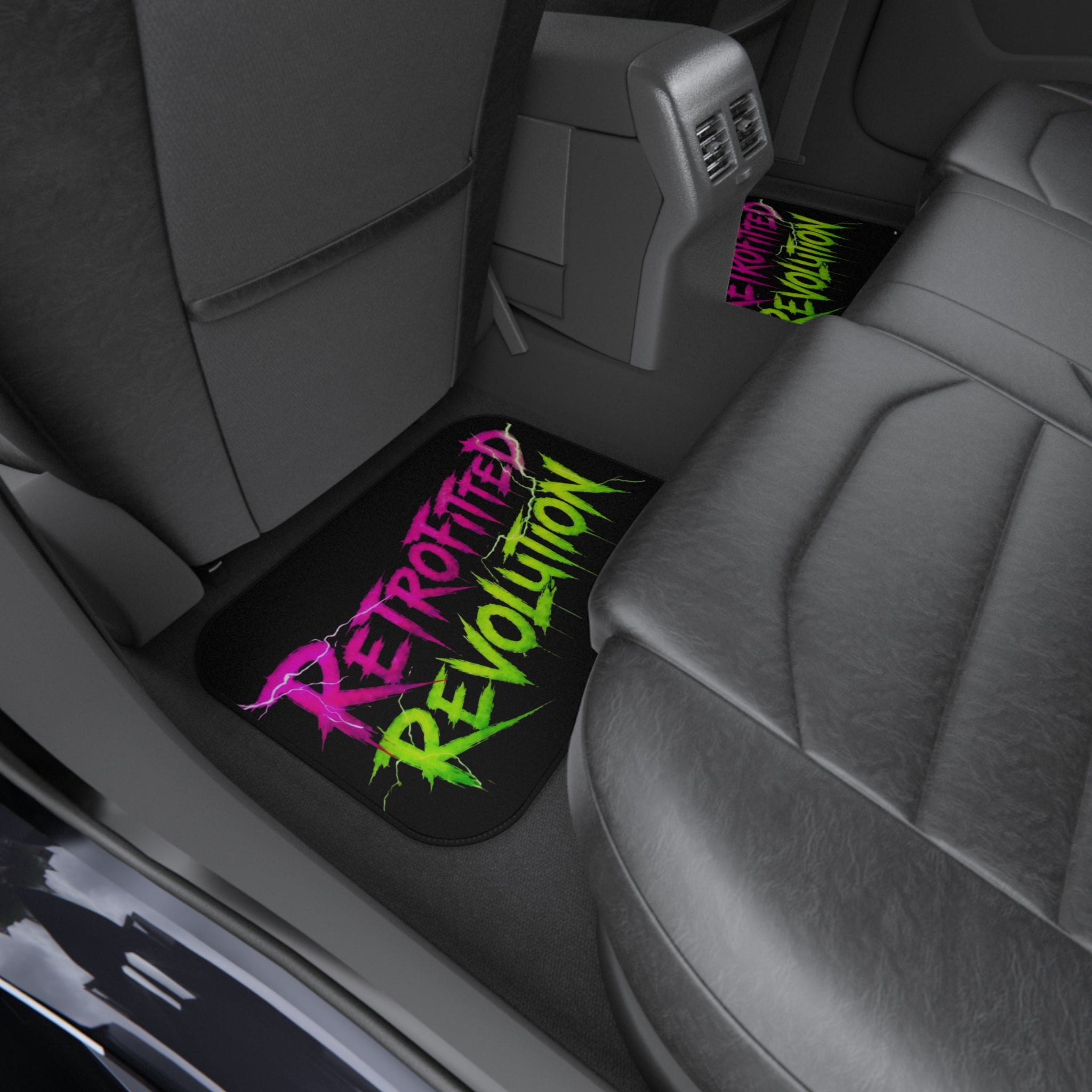 Car mats featuring vibrant graffiti-style "RETROFITTED REVOLUTION" text in a vehicle interior with dark upholstery.