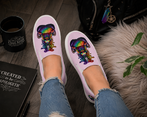 Vibrant rainbow Medusa slip-on canvas shoes on a textured surface with a notebook, coffee cup, and plant nearby.