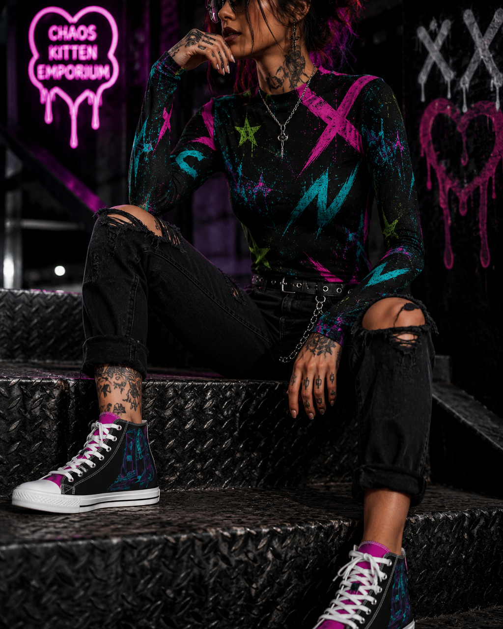 Model wearing a fitted black long-sleeve top with vibrant graffiti print, styled with distressed black jeans and colorful sneakers.
