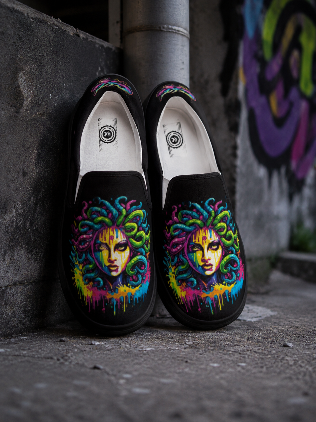 Black loafers with colorful face designs leaning against a wall with graffiti.