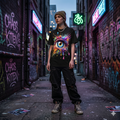 Model wearing the Vivid Iris surrealist graphic tee in a gritty urban alleyway, styled with streetwear cargo pants and beanie, showcasing the electric color contrast of the design.
